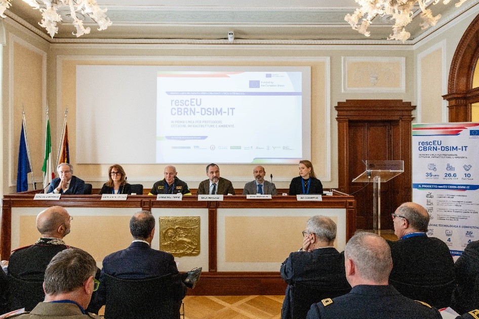 Foto della sala dove è avvenuta la presentazione del lancio pubblico di rescEU-CBRN-DSIM-IT presso il Palazzo della Regione, Venezia, immagine della sala del convegno con personalità presenti all'evento. Tavolo con relatori e slide di sfondo che accompagna la presentazione